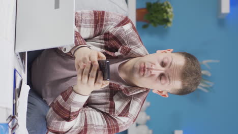 Vertical-video-of-Man-working-from-home-enjoys-mobile-apps-on-phone.